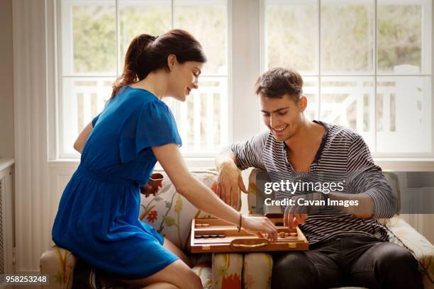 couple playing backgammon while sitting on armchair at home - backgammon stockfoto's en -beelden