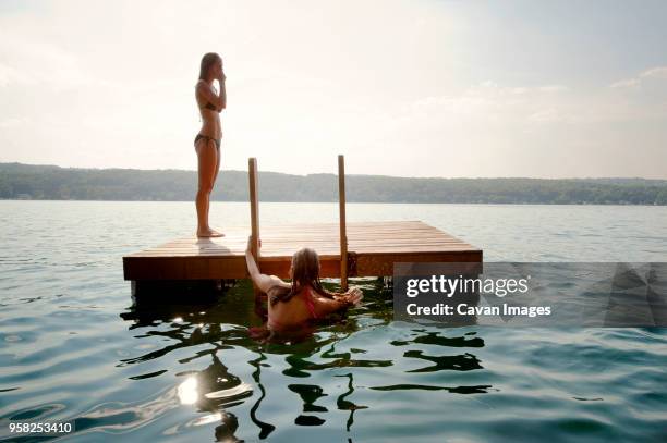 friends at floating platform in lake against sky on sunny day - schwimmende plattform stock-fotos und bilder