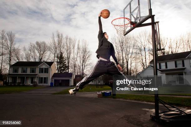 boy dunking ball in hoop on road - slam dunk stock pictures, royalty-free photos & images