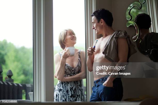 woman with coffee cup talking to man leaning on wall by window at home - coffee cup top view stockfoto's en -beelden