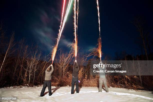 rear view of male friends holding sparklers on snow covered field at dusk - cavan images stockfoto's en -beelden