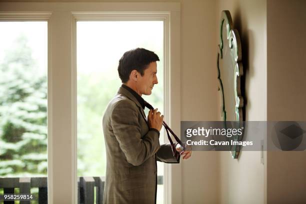 side view of man adjusting tie while looking at mirror - adjusting suit stock pictures, royalty-free photos & images