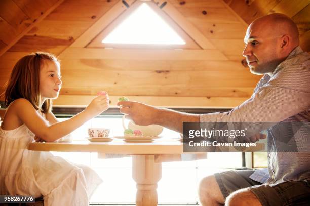 father and daughter holding cupcakes while sitting at table - cupcake teacup stockfoto's en -beelden