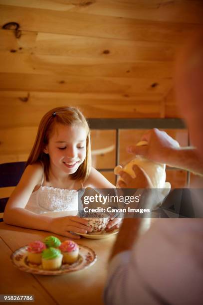 cropped image of father serving tea to happy daughter while sitting at table - cupcake teacup stock-fotos und bilder