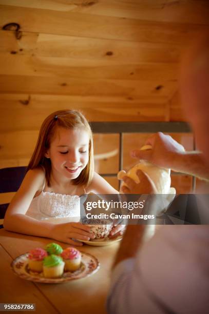 cropped image of father serving tea to happy daughter while sitting at table - cupcake teacup stockfoto's en -beelden