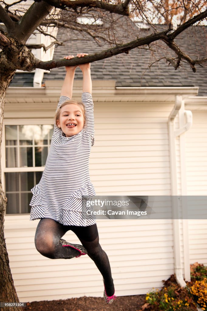 Low angle view of cheerful girl hanging from tree in yard