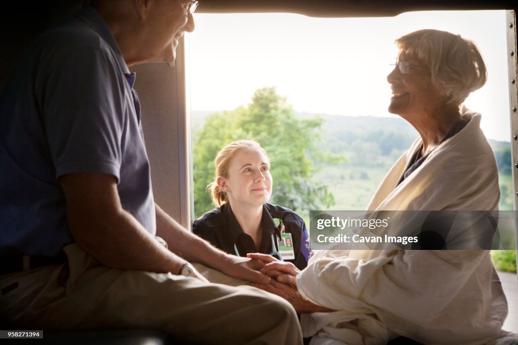 Paramedic looking at patient sitting with husband in ambulance