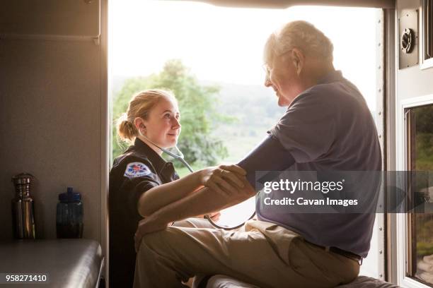 paramedic checking mans blood pressure in ambulance - medical ambulance female stockfoto's en -beelden