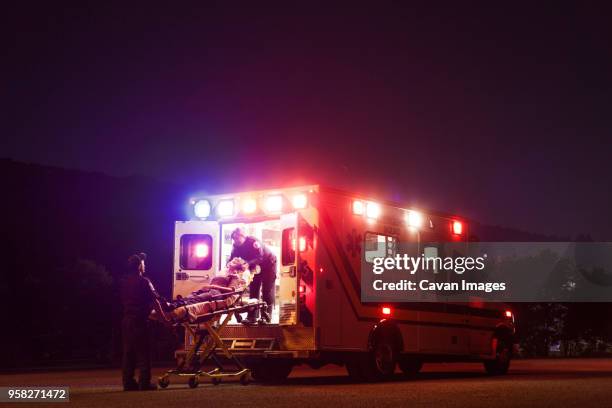 paramedics carrying patient in ambulance at night - ambulance stockfoto's en -beelden