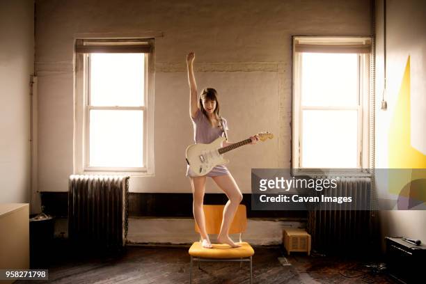 happy woman playing guitar while standing on chair at home - woman playing guitar stock pictures, royalty-free photos & images