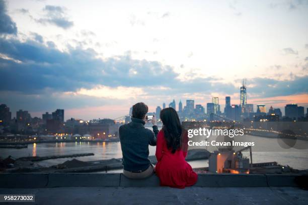 rear view of couple clicking photograph of illuminated cityscape at dusk - indian ethnicity travel stock pictures, royalty-free photos & images