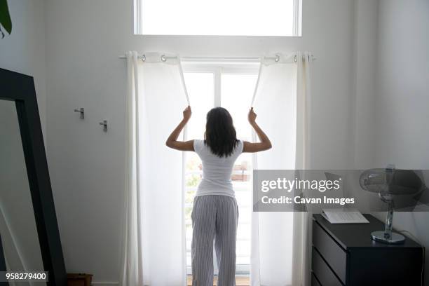 rear view of woman closing curtain at home - closing curtains stock pictures, royalty-free photos & images