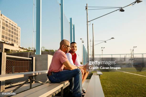 happy father and son sitting on bleachers at soccer field - old american football fotografías e imágenes de stock