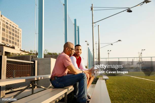 happy father and son sitting on bleachers at soccer field - urban football pitch stock pictures, royalty-free photos & images