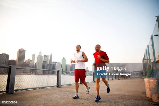 happy man and father jogging on promenade by east river in city against clear sky - east river stock-fotos und bilder