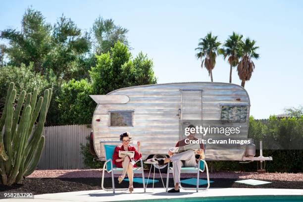 couple reading newspaper while sitting on chair against camper van - zeitung lesen zwei personen stock-fotos und bilder