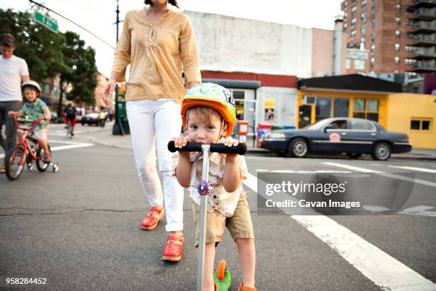 portrait of boy riding push scooter with family on streets in city - center street elementary - fotografias e filmes do acervo