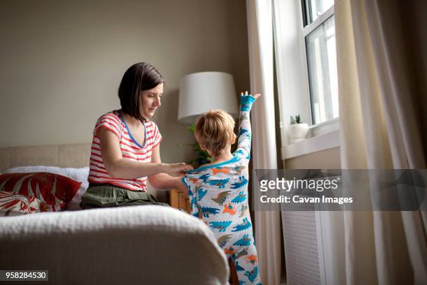 mother dressing son while sitting on bed in room - kids dressing up stock-fotos und bilder