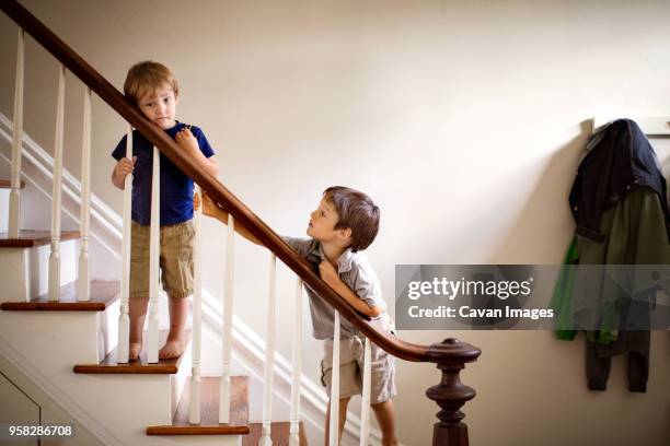 brothers standing at railing of staircase in house - step brother stock pictures, royalty-free photos & images