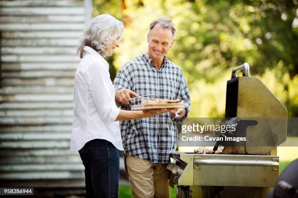happy senior couple preparing food while standing by barbecue grill in backyard - baby boomer stock pictures, royalty-free photos & images