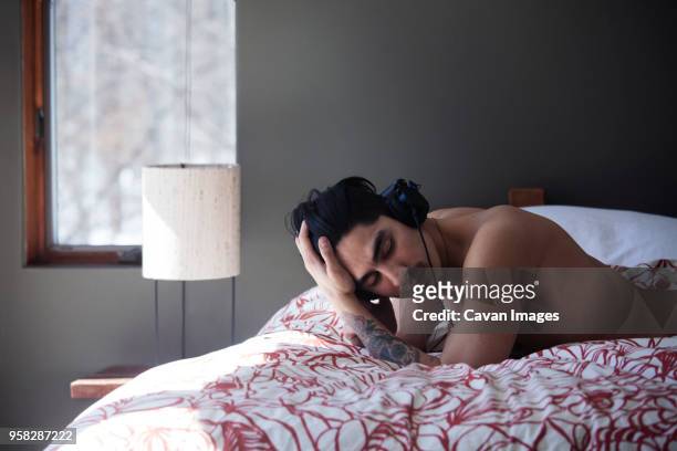 shirtless man with hand in hair listening music while lying in bed - male hair hand ストックフォトと画像