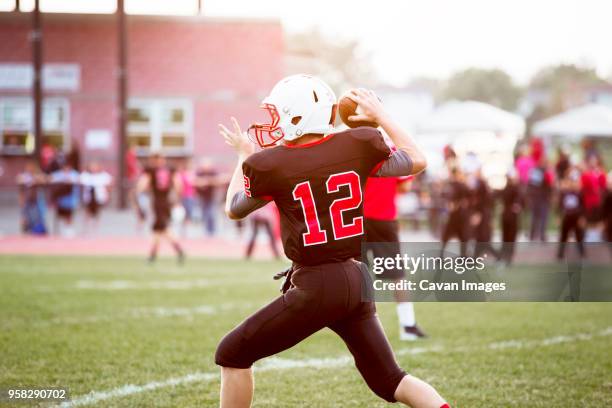 rear view of quarterback throwing football on playing field - quarterback teenager stock pictures, royalty-free photos & images