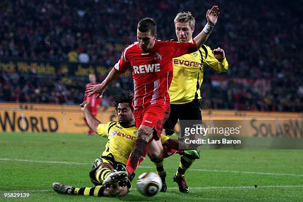 Lukas Podolski of Koeln is challenged by Patrick Owomoyela and Jakub Blaszczykowski of Dortmund during the Bundesliga match between 1. FC Koeln and...