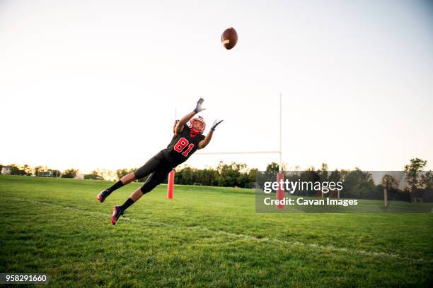 young man diving to catch american football at playing field against sky - safety american football player imagens e fotografias de stock