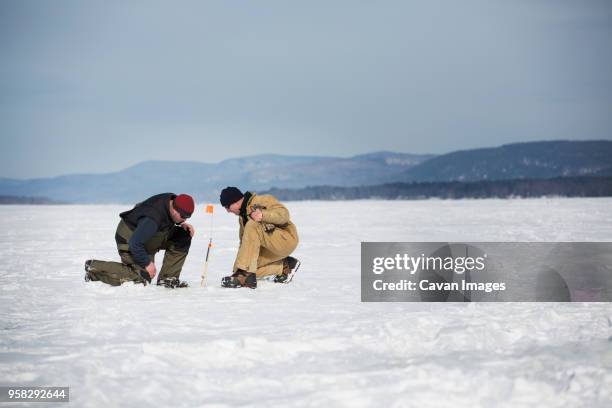 side view of men ice fishing on frozen lake against sky - winter testing imagens e fotografias de stock