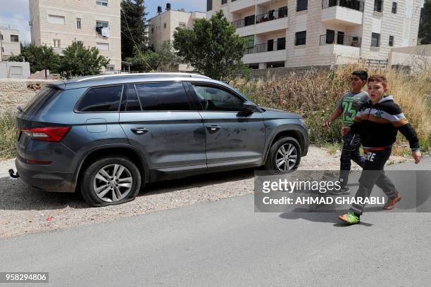 Palestinian children walk by a car whose tyres were slashed in the latest "price tag" attack in the Palestinian neighborhood of Shuafat in Israeli...