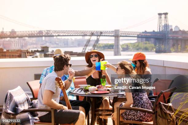 friends enjoying breakfast party on building terrace against williamsburg bridge - bridge building glass stock pictures, royalty-free photos & images