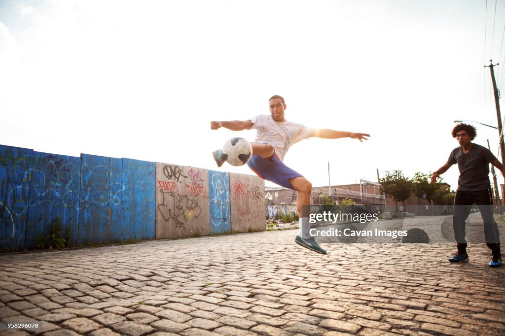 Man kicking soccer ball while friend looking at street