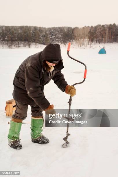 senior man drilling in frozen lake - russia rain boots imagens e fotografias de stock