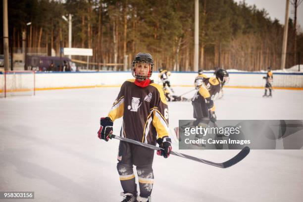 portrait of player holding ice hockey stick while standing on rink - kids ice hockey stock pictures, royalty-free photos & images