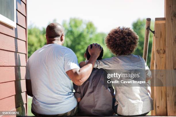 rear view of father with children sitting at backyard - family from behind stock pictures, royalty-free photos & images