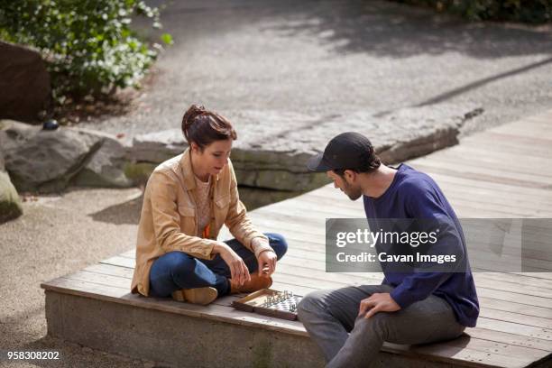 high angle view of couple playing chess while sitting on floorboard in lawn - chess rock stock pictures, royalty-free photos & images