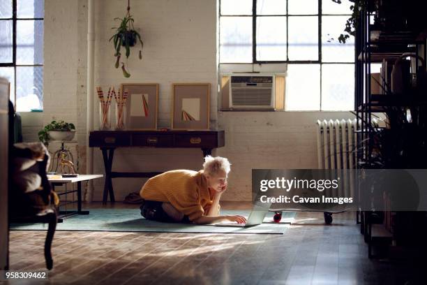 woman using laptop computer while kneeling on floor at home - cavan images stockfoto's en -beelden