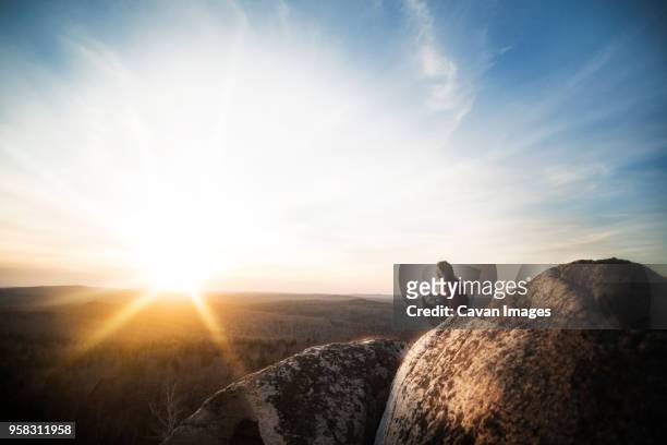 side view of woman sitting on rocks at cliff against sky during sunset - cliff side stock pictures, royalty-free photos & images
