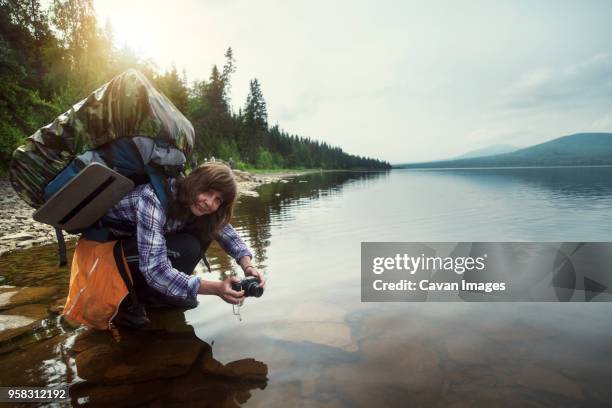 portrait of female hiker crouching at lake - heavy rucksack stock pictures, royalty-free photos & images