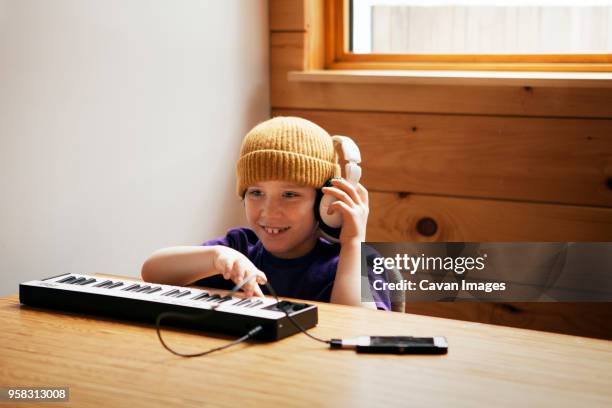 boy playing keyboard piano while sitting at table in home - keyboard instrument stock pictures, royalty-free photos & images