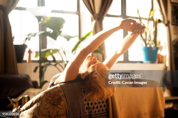 woman stretching while leaning on sofa - relief foto e immagini stock