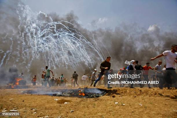 Palestinians run for cover from tear gas during clashes with Israeli security forces near the border between Israel and the Gaza Strip, east of...