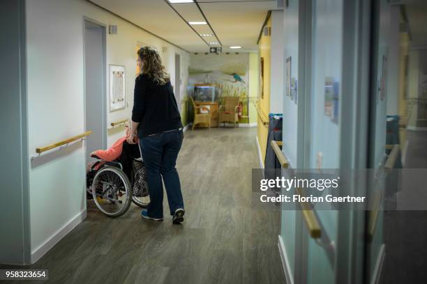 Caregiver pushes an older woman in a wheelchair through a corridor in a care facility on April 27, 2018 in Berlin, Germany.