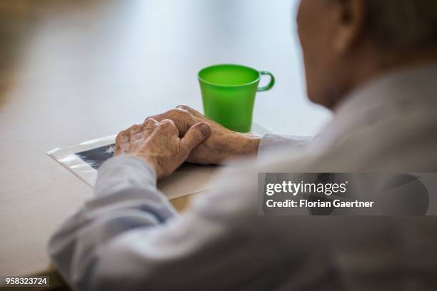 An old man sits alone at a table. His hands lay on an old photo on April 27, 2018 in Berlin, Germany.