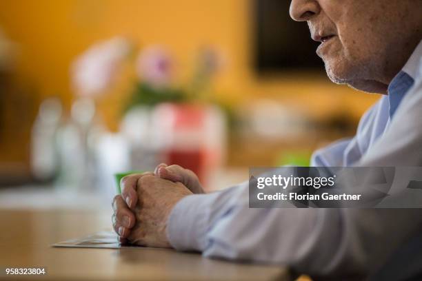 An old man sits alone at a table. His hands lay on an old photo on April 27, 2018 in Berlin, Germany.