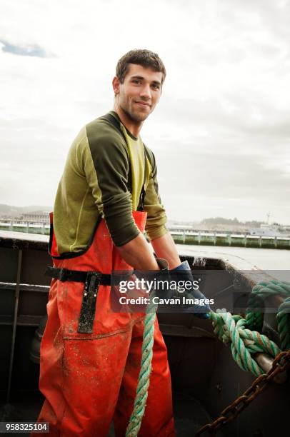 portrait of smiling fisherman pulling rope on fishing boat against sky - fisherman stockfoto's en -beelden