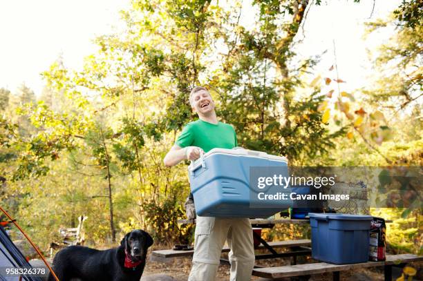 happy man carrying cooler while standing by dog at campsite - kühlbehälter stock-fotos und bilder