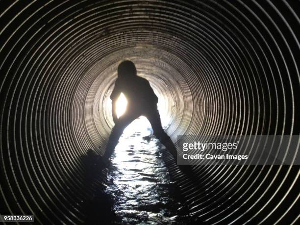 rear view of silhouette boy standing in sewage tunnel - égout photos et images de collection