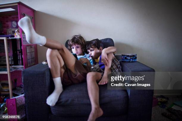 sibling using handheld video game while sitting on sofa at home - video wall fotografías e imágenes de stock