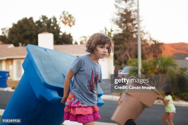 girl pulling garbage can while walking on road - mülleimer auf rollen stock-fotos und bilder